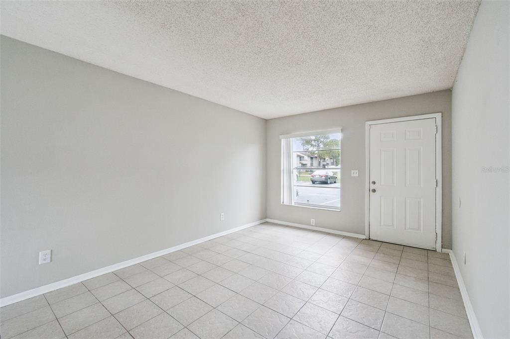 An empty room with light gray walls, tiled flooring, a window, and a white door — 2 LAKE VILLA WAY, KISSIMMEE, FL