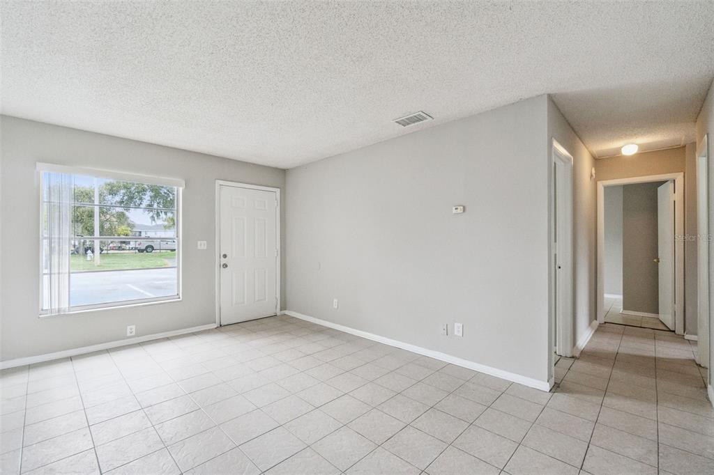 A living room with light gray walls, white tile flooring, a window, and a front door — 2 LAKE VILLA WAY, KISSIMMEE, FL