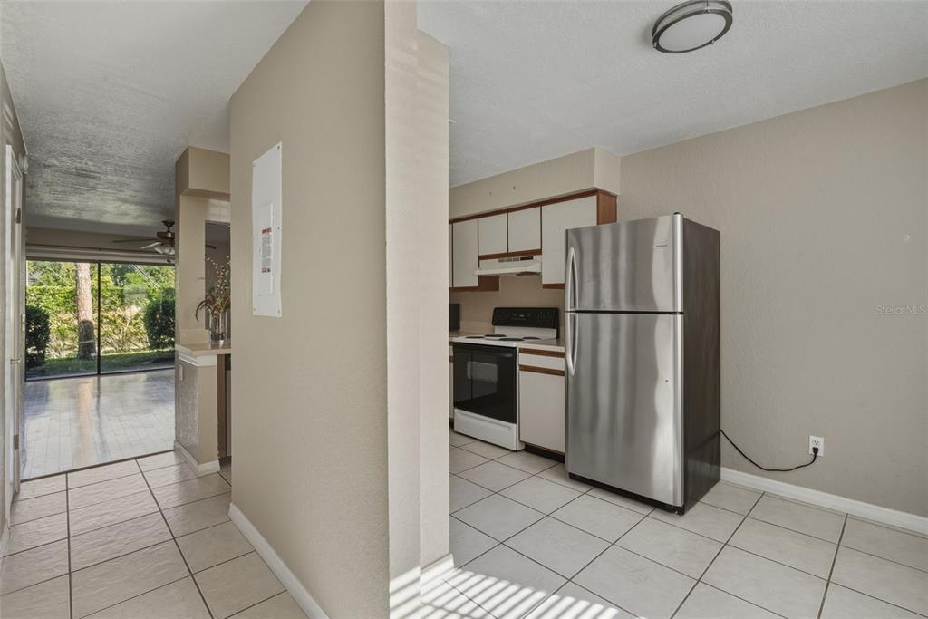 A kitchen with white cabinets, stainless steel appliances, and tile flooring opens to a living area — 16545 LAKE BRIGADOON CIRCLE, TAMPA, FL