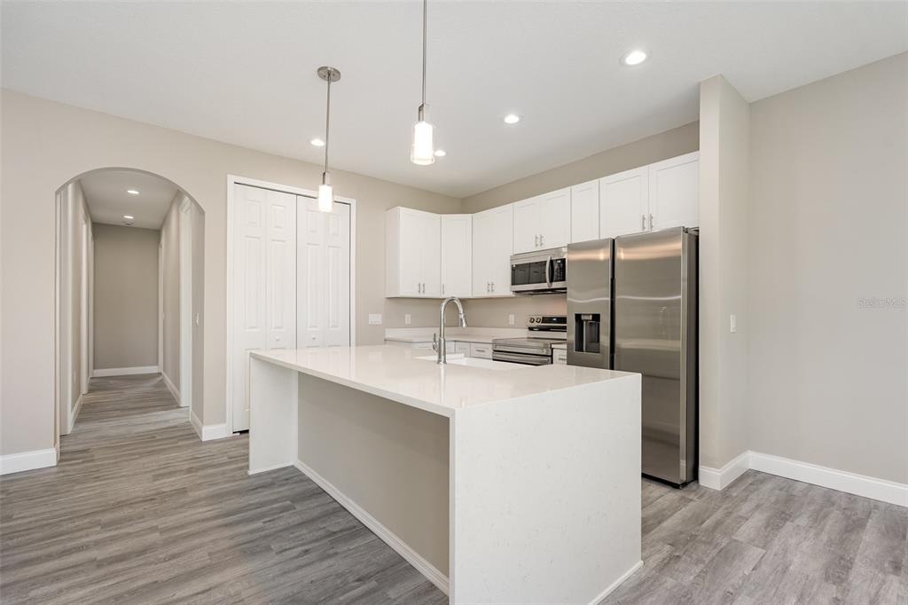A modern kitchen features a white quartz island, stainless steel appliances, and light gray flooring — 1041 WESBERRY STREET SE, PALM BAY, FL