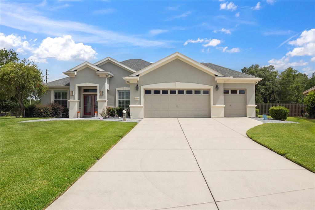 A single-story house with a gray stucco exterior, a three-car garage, and a concrete driveway — 13944 SE 96TH CIRCLE, SUMMERFIELD, FL