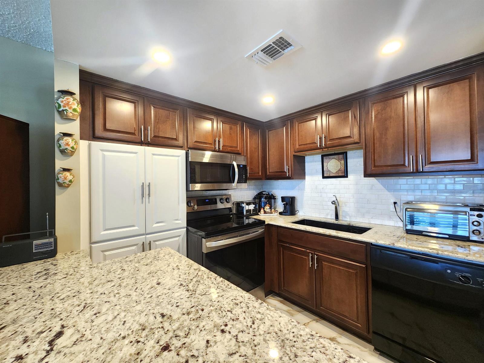 A kitchen features dark wood cabinets, white subway tile backsplash, and granite countertops — 1012 Ellesmere A # 1012, Deerfield Beach FL 33442, DEERFIELD BEACH, FL