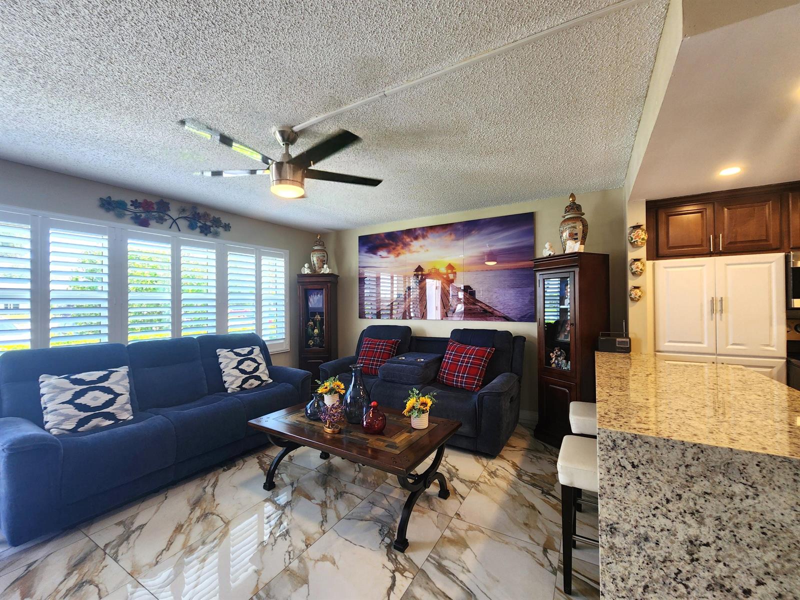 A living room features blue sofas, a coffee table, and marble flooring near a kitchen — 1012 Ellesmere A # 1012, Deerfield Beach FL 33442, DEERFIELD BEACH, FL