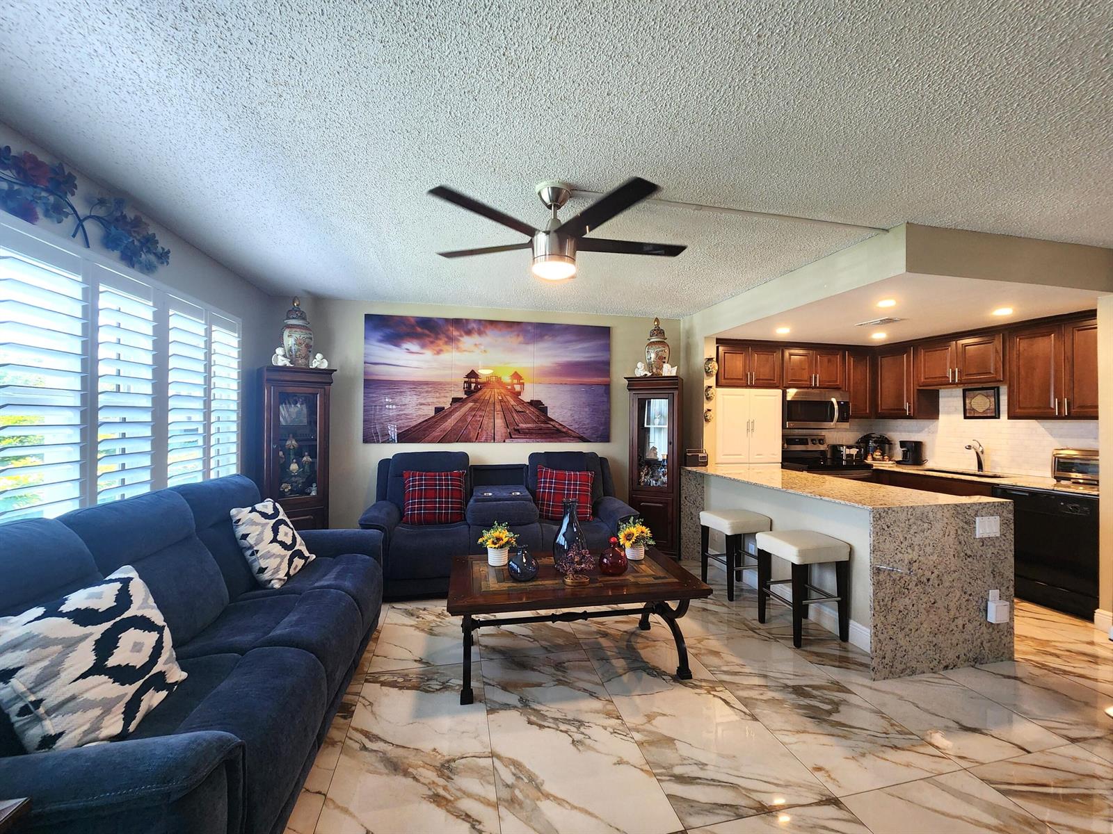 A living room with blue sofas, a coffee table, and an open kitchen with granite counters — 1012 Ellesmere A # 1012, Deerfield Beach FL 33442, DEERFIELD BEACH, FL