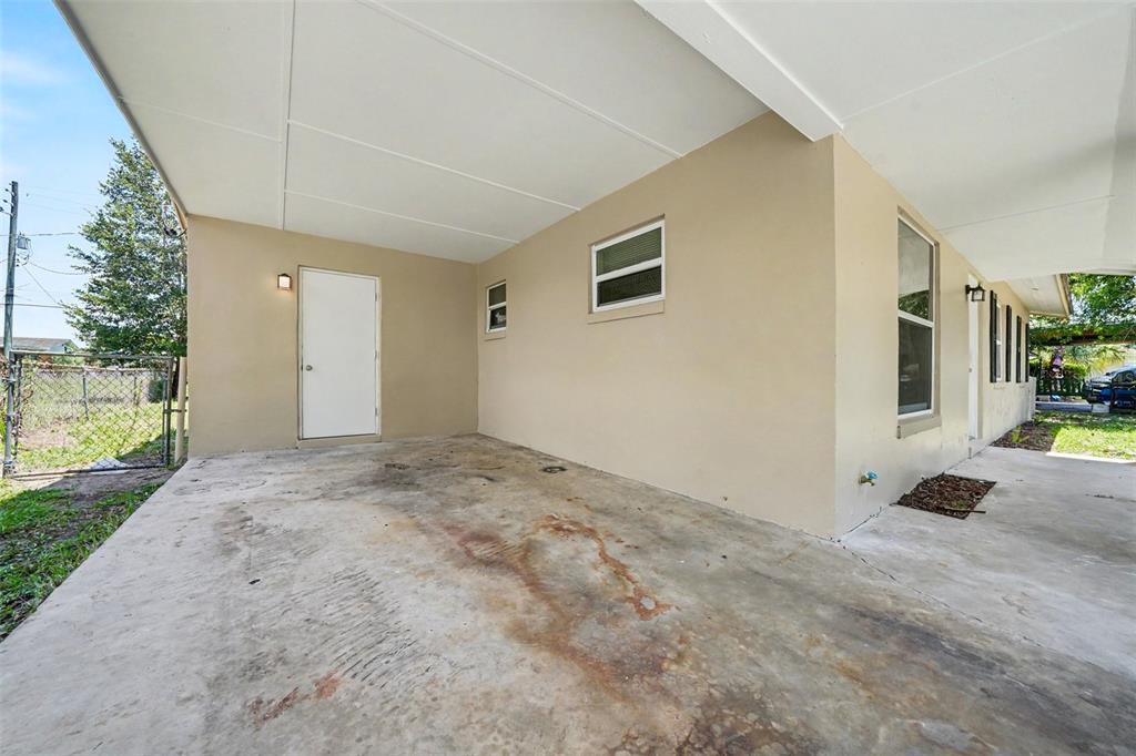 A concrete carport attached to a house with a white door and two windows — 1895 S IVEY LANE, ORLANDO, FL