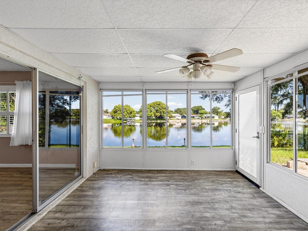 A sunroom with wood-look flooring, a ceiling fan, and large windows overlooking a lake — 4135 COTTON TAIL DRIVE, NEW PORT RICHEY, FL