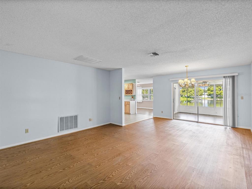 A spacious living room features wood-look flooring, a sliding glass door, and a view of water — 4135 COTTON TAIL DRIVE, NEW PORT RICHEY, FL