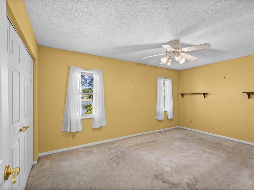 An empty bedroom with yellow walls, beige carpet, two windows, and a ceiling fan — 4135 COTTON TAIL DRIVE, NEW PORT RICHEY, FL