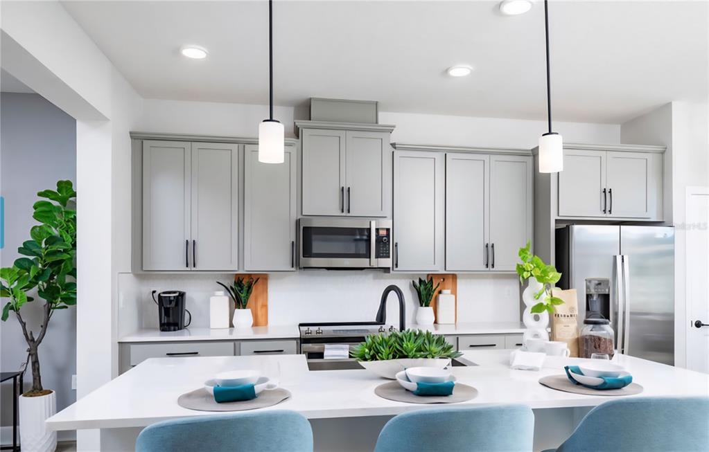 A kitchen features gray cabinets, stainless steel appliances, a white island, and light blue chairs — 15212 TRIBUTE OVATION WAY, WINTER GARDEN, FL