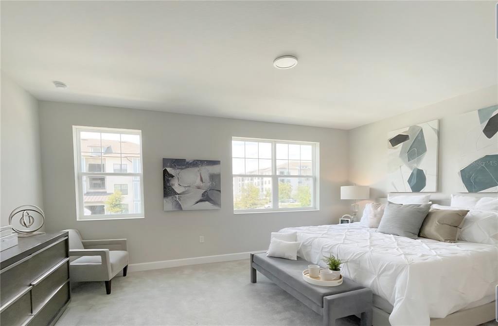 A bedroom features a bed with white bedding, a gray bench, and two windows — 15212 TRIBUTE OVATION WAY, WINTER GARDEN, FL