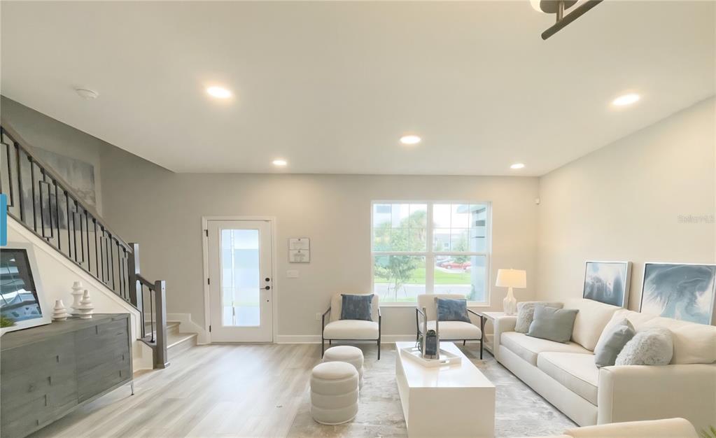 A bright living room features light wood-look flooring, a white sofa, and a staircase — 15212 TRIBUTE OVATION WAY, WINTER GARDEN, FL
