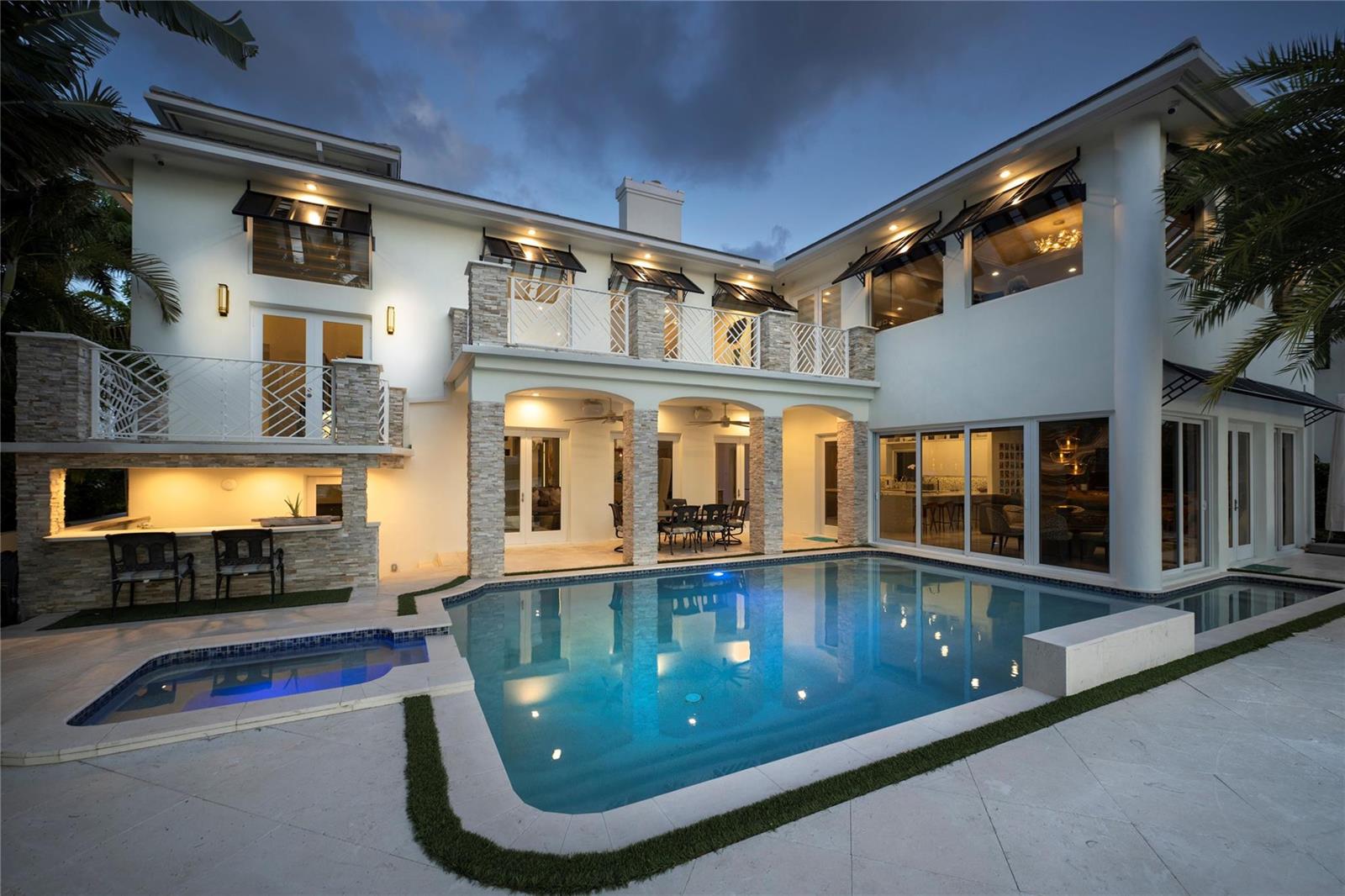 A two-story house with a swimming pool, stone columns, and a second-floor balcony at dusk — 2307 N Riverside Drive, Pompano Beach FL 33062, POMPANO BEACH, FL