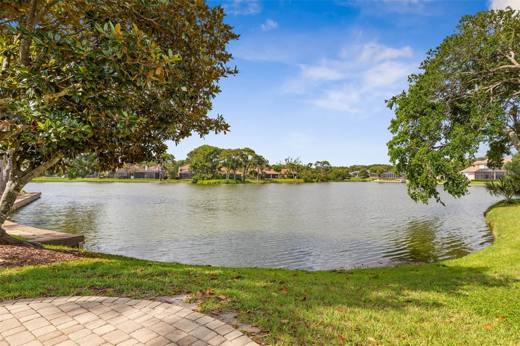 A view of a lake from a paved patio surrounded by grass and trees — 16 MARBELLA COURT, PALM COAST, FL