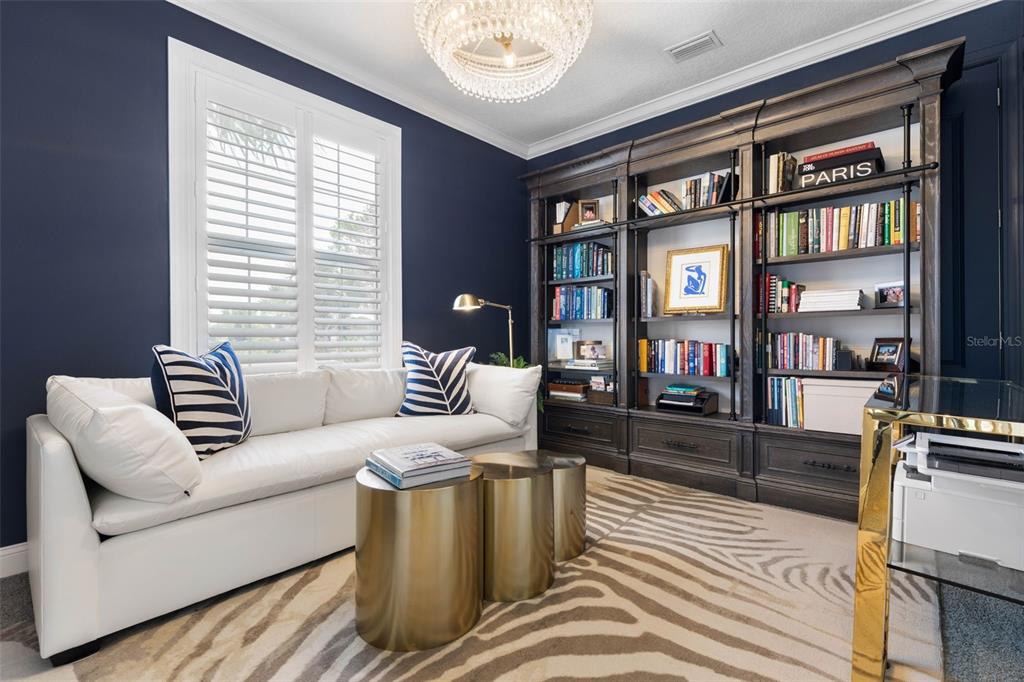 A home office features a white sofa, gold coffee tables, dark bookshelves, and a zebra-print rug — 16 MARBELLA COURT, PALM COAST, FL