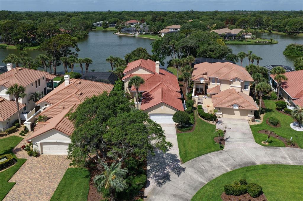 An aerial view shows three suburban houses with tile roofs near a lake — 16 MARBELLA COURT, PALM COAST, FL
