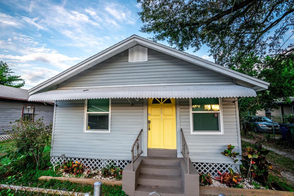 A gray house with a bright yellow front door, metal awning, and lattice skirting — 4811 N 30TH STREET, TAMPA, FL