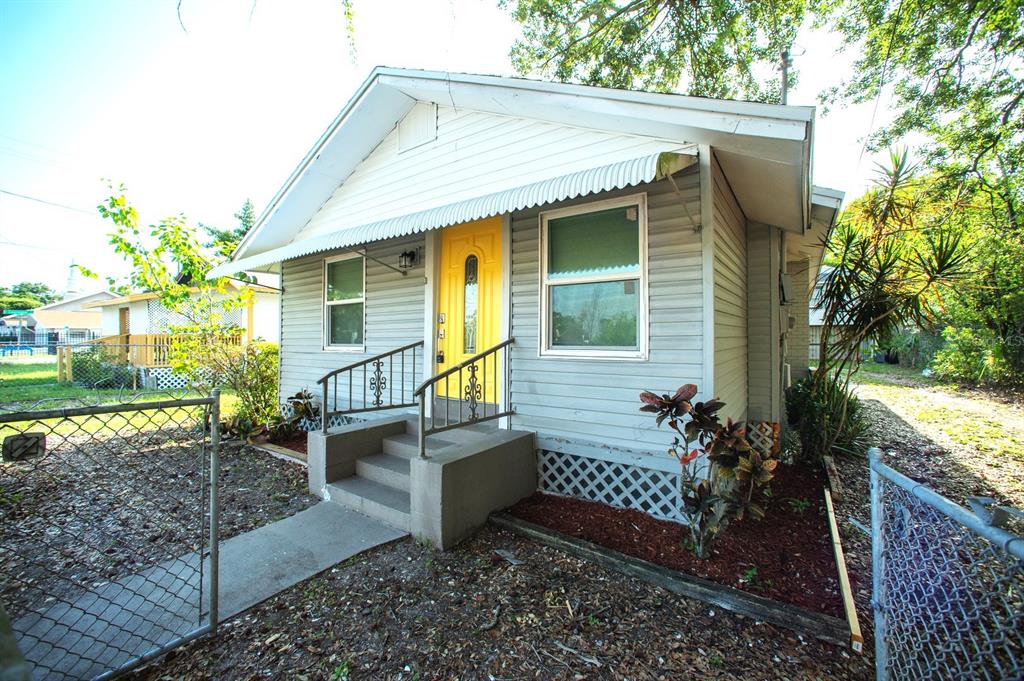 A small, light-gray siding house with a bright yellow front door and metal window awnings — 4811 N 30TH STREET, TAMPA, FL