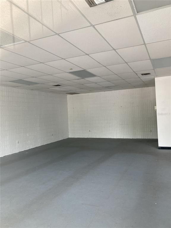 An empty commercial space features white painted brick walls, a drop ceiling, and gray flooring — 2020 NW 6TH STREET, GAINESVILLE, FL
