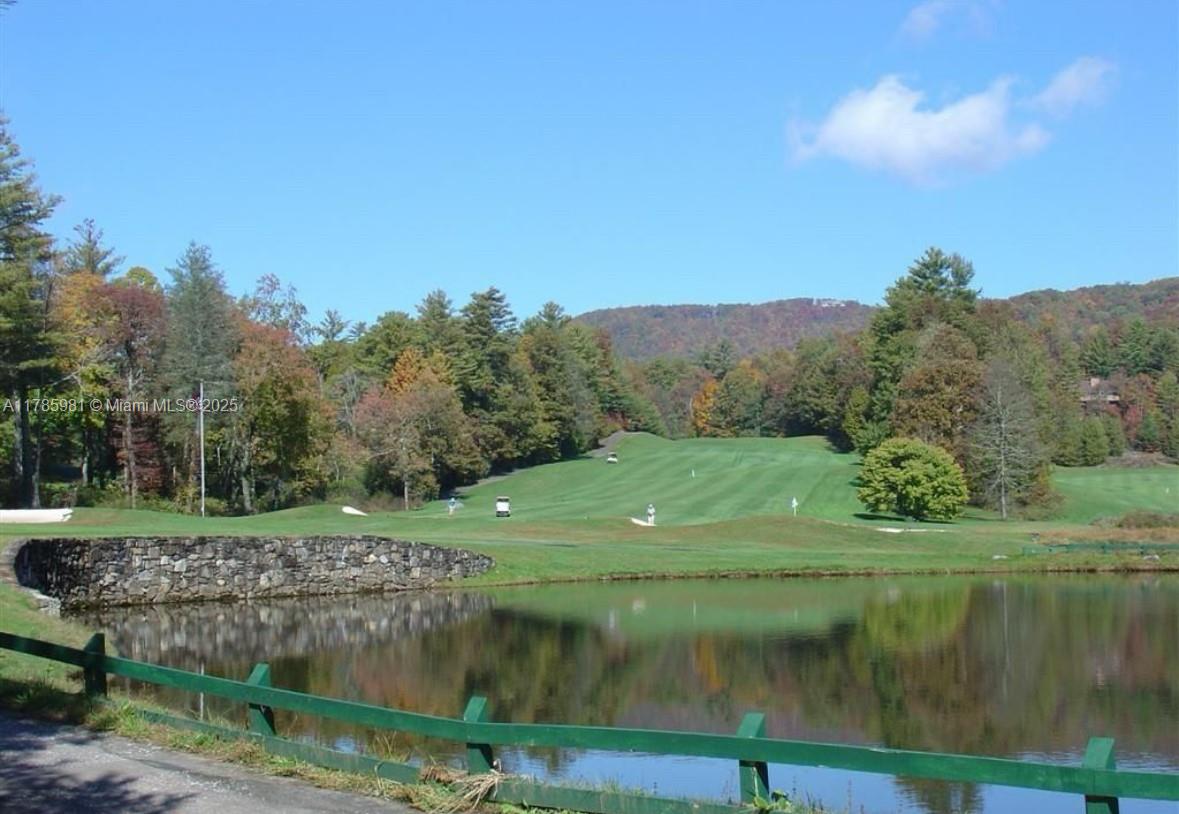 A golf course fairway stretches toward a forested mountain behind a pond and stone wall — Lot 66 Juniper Court, NC 28774, NC