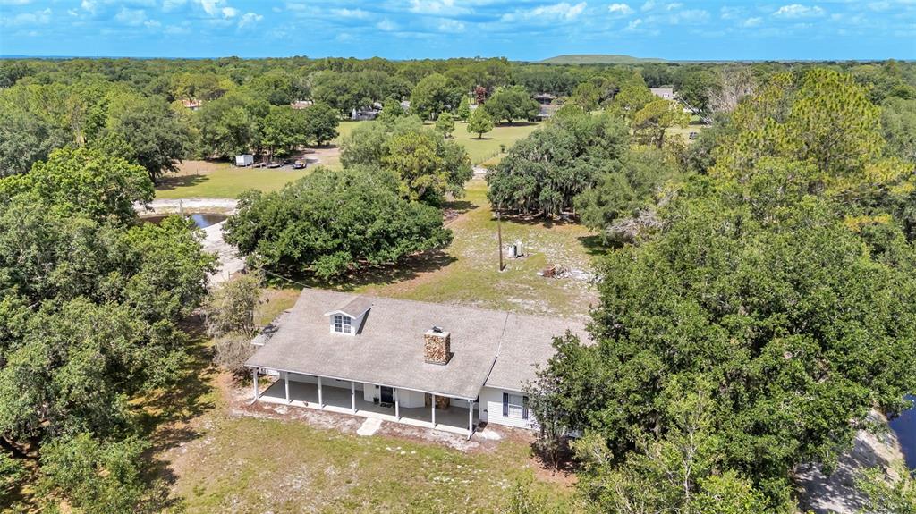 An aerial view shows a single-story house with a wrap-around porch and stone chimney — 29 LAKE ARROWHEAD DRIVE, WINTER HAVEN, FL
