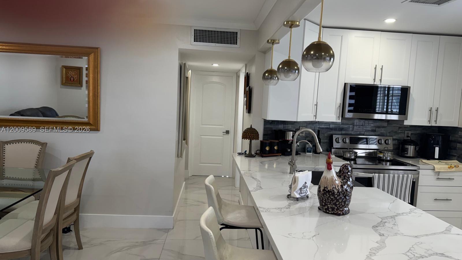 A kitchen features white cabinets, a marble-patterned island with bar stools, and a dining area — 31 Normandy A # A, Delray Beach FL 33484, DELRAY BEACH, FL
