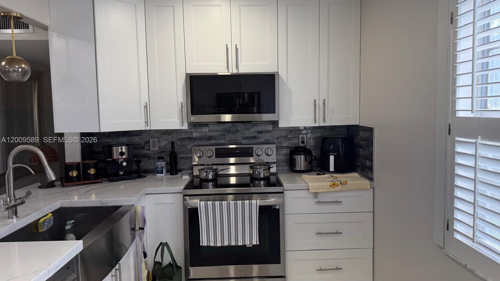 A kitchen features white cabinets, stainless steel appliances, and a dark gray tiled backsplash — 31 Normandy A # A, Delray Beach FL 33484, DELRAY BEACH, FL