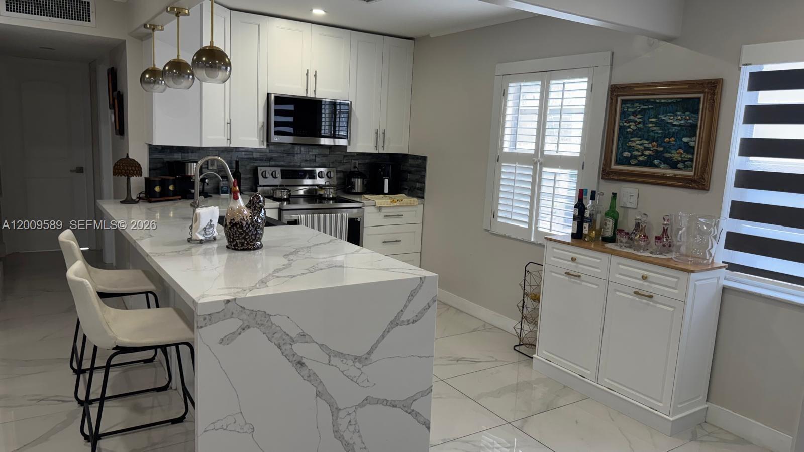 A modern kitchen features white cabinets, a marble waterfall island, and stainless steel appliances — 31 Normandy A # A, Delray Beach FL 33484, DELRAY BEACH, FL