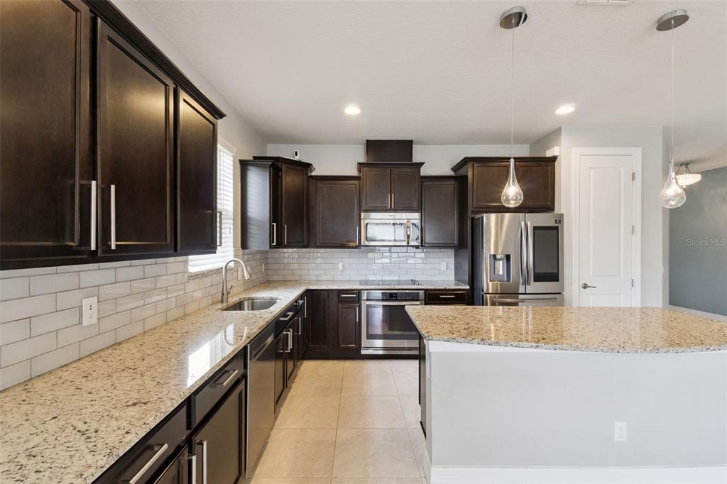 A kitchen features dark wood cabinets, granite countertops, stainless steel appliances, and a center island — 2651 TAHOE TERRACE, ST CLOUD, FL