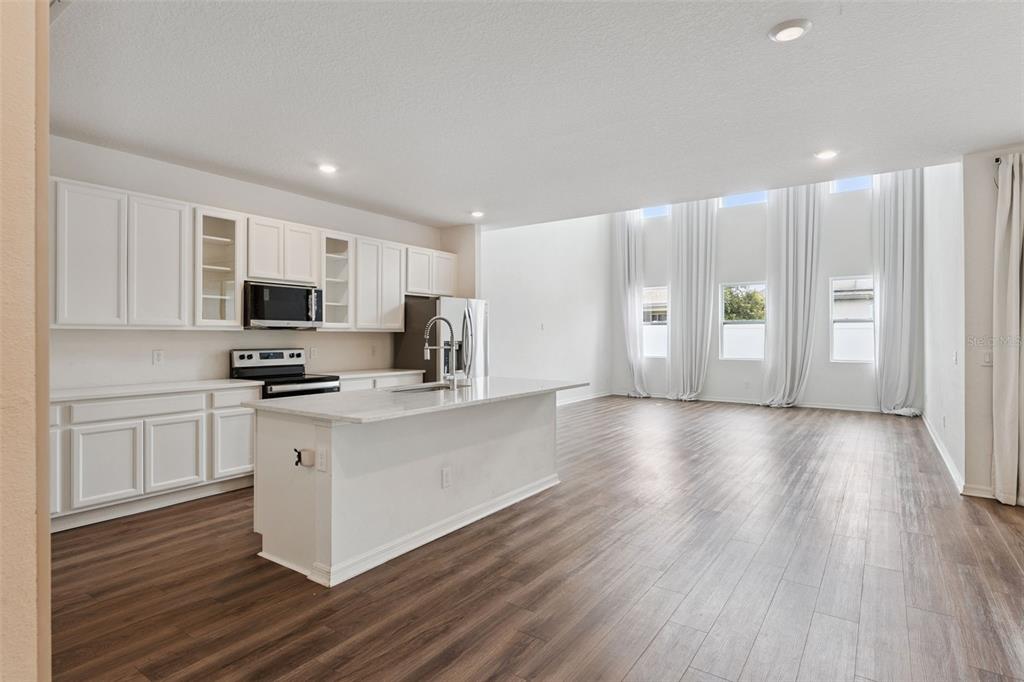 A kitchen with white cabinets and a center island opens into a high-ceilinged living area — 756 STEERVIEW STREET, ST CLOUD, FL