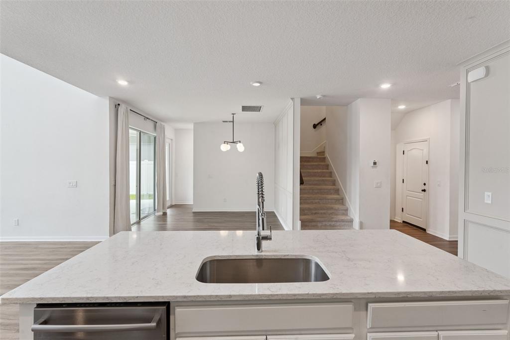 A kitchen island with a stainless steel sink overlooks an open living area and staircase — 756 STEERVIEW STREET, ST CLOUD, FL