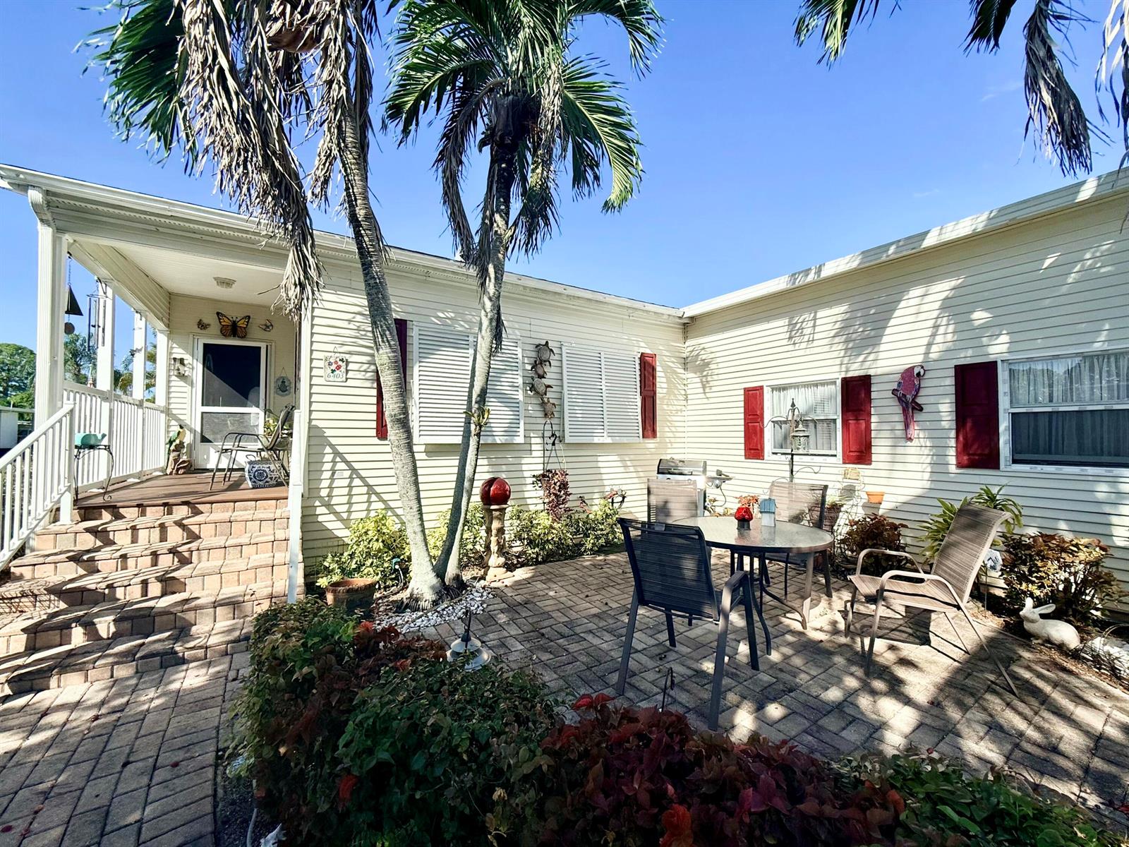 A paved patio with outdoor furniture sits beside a house with light siding and shutters — 6403 Birch Lane, Lantana FL 33462, LANTANA, FL