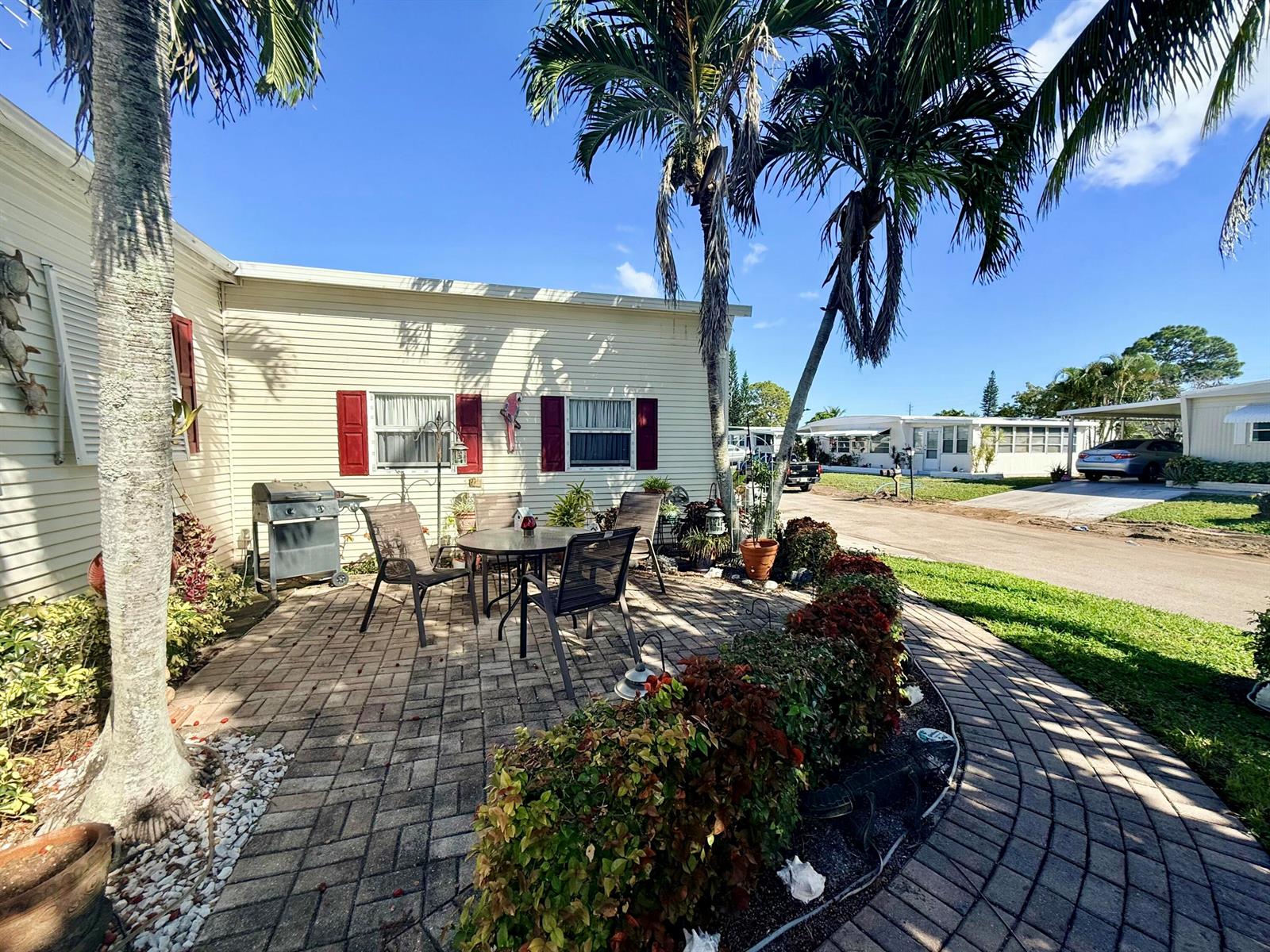 A patio with a dining set and grill sits beside a house with palm trees — 6403 Birch Lane, Lantana FL 33462, LANTANA, FL