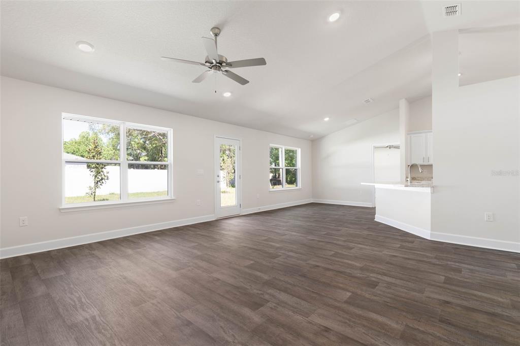 A spacious living room with wood-look flooring, a ceiling fan, and an open kitchen area — 105 PALMWOOD DRIVE, PALM COAST, FL