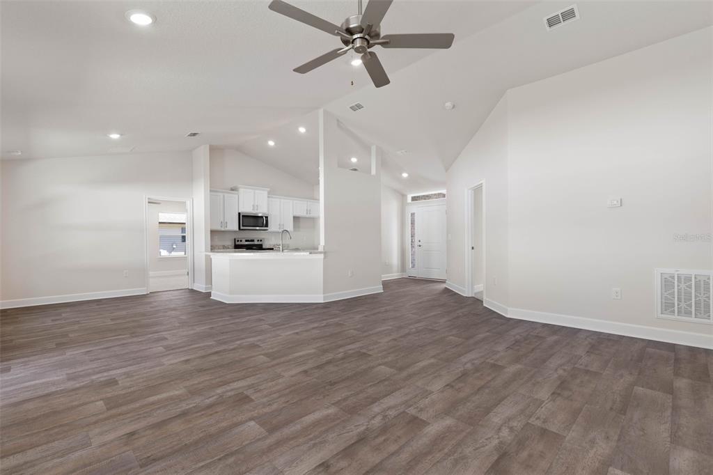 An open-concept living area features vaulted ceilings, wood-look flooring, and a kitchen with white cabinets — 105 PALMWOOD DRIVE, PALM COAST, FL