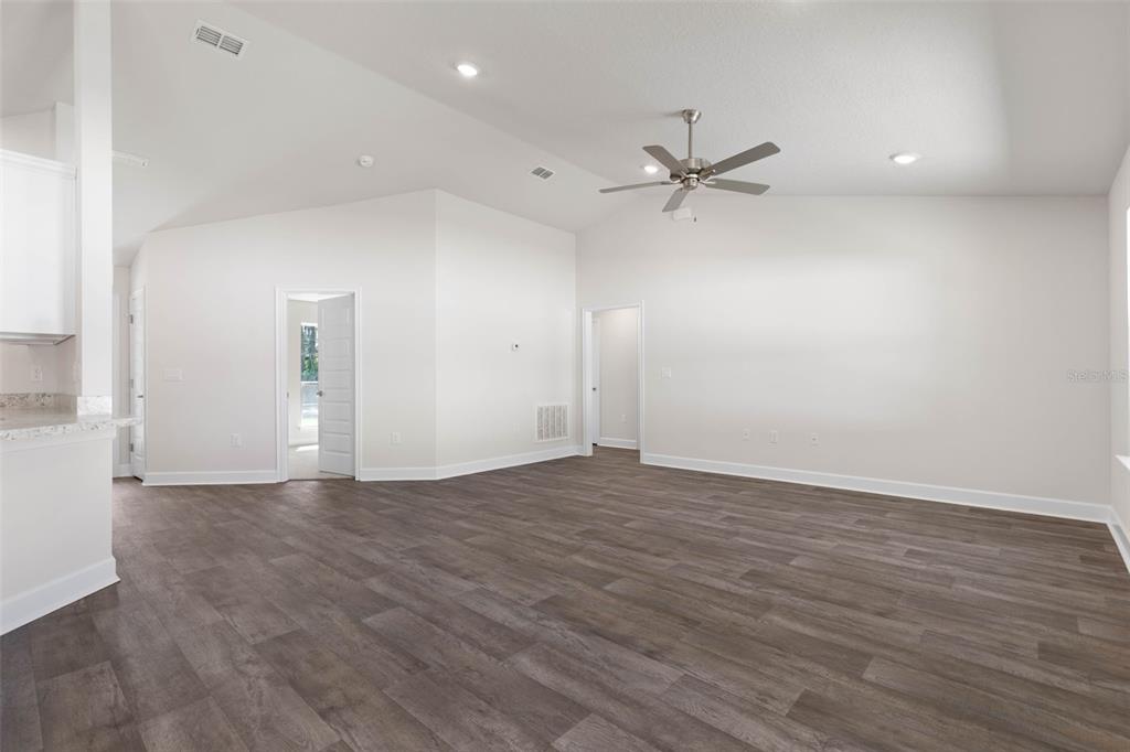 An empty living room features vaulted ceilings, a ceiling fan, and wood-look vinyl flooring — 105 PALMWOOD DRIVE, PALM COAST, FL