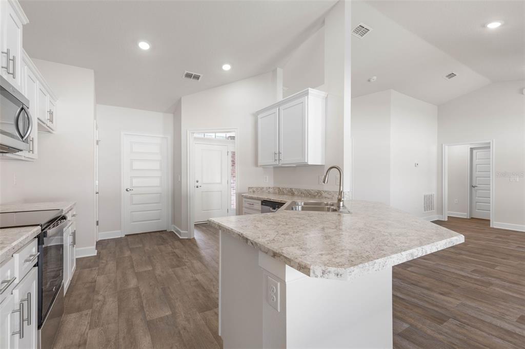 A kitchen with white cabinets, granite countertops, stainless steel appliances, and wood-look flooring — 105 PALMWOOD DRIVE, PALM COAST, FL
