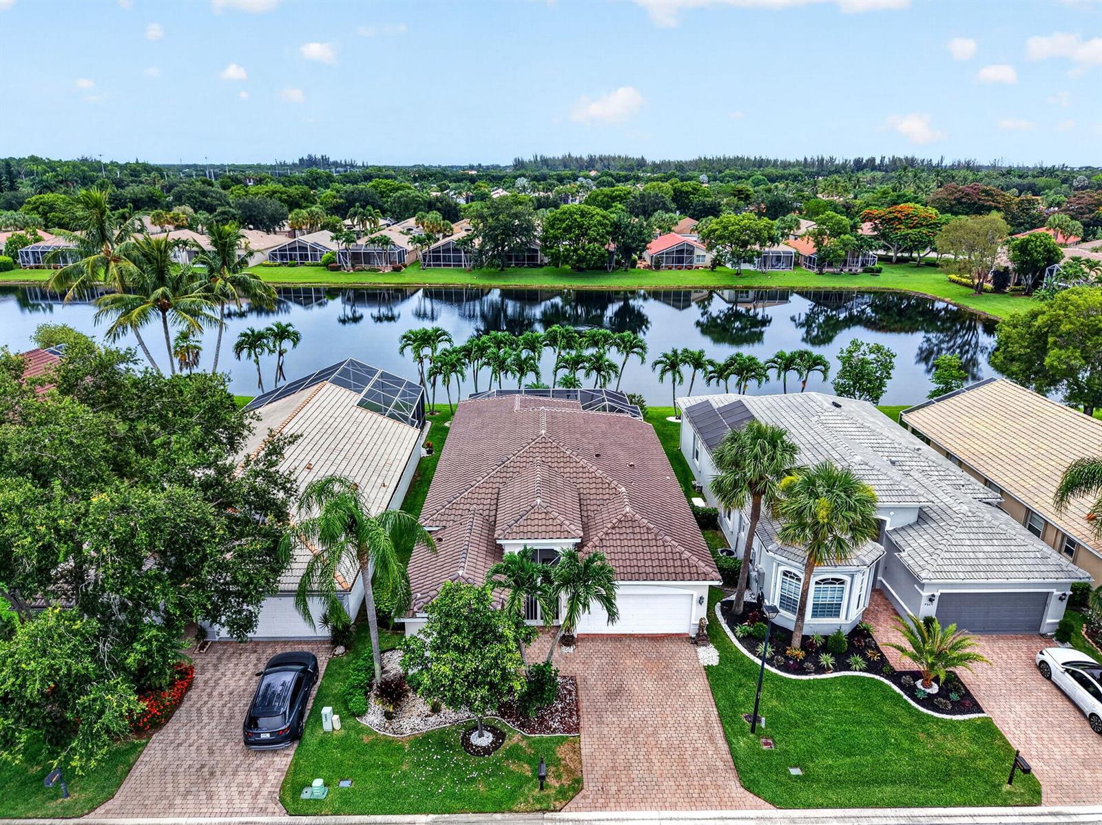 An aerial view shows three suburban houses with tiled roofs situated along a lake — 9871 Agnello Street, Lake Worth FL 33467, LAKE WORTH, FL