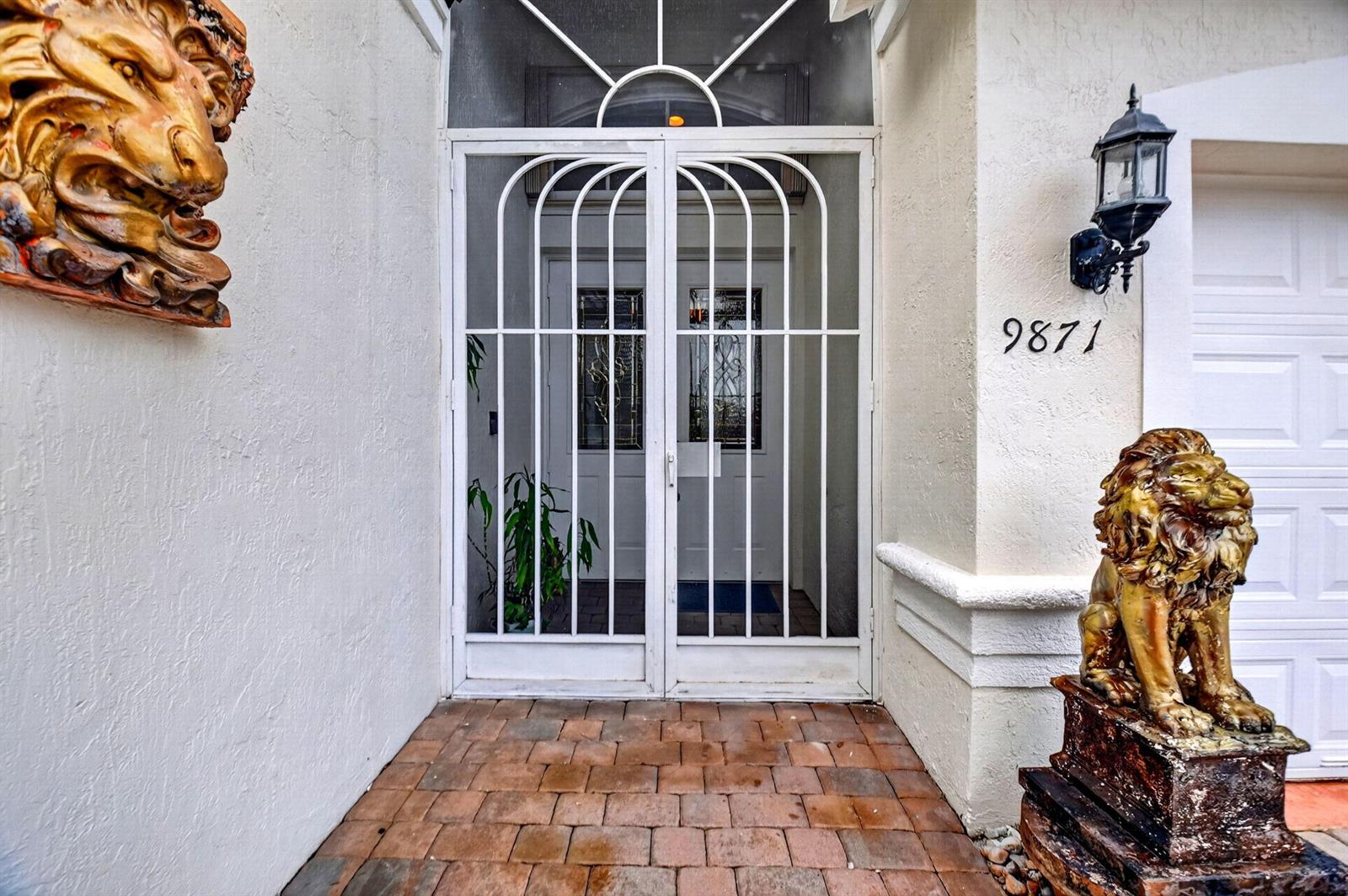 A front entryway features a white metal security door, lion statues, and brick pavers — 9871 Agnello Street, Lake Worth FL 33467, LAKE WORTH, FL