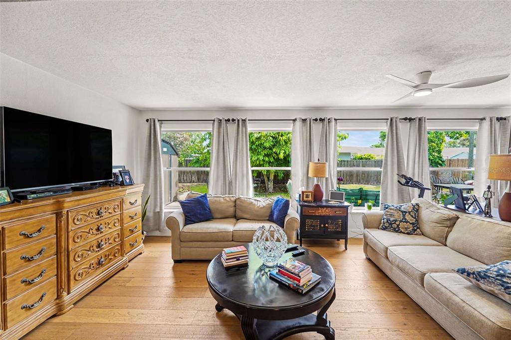 A living room features a television on a wooden dresser, two sofas, and large windows — 6825 11TH AVENUE N, ST PETERSBURG, FL