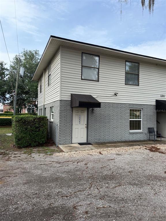 A two-story building with light siding, a gray brick lower level, and a gravel parking area — 131 W BROADWAY STREET UNIT 1001, OVIEDO, FL