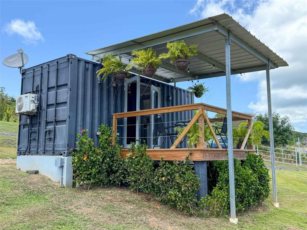 A shipping container home features a wooden deck, a metal roof, and hanging potted plants — 324 CAMINO SOL, VIEQUES, PR