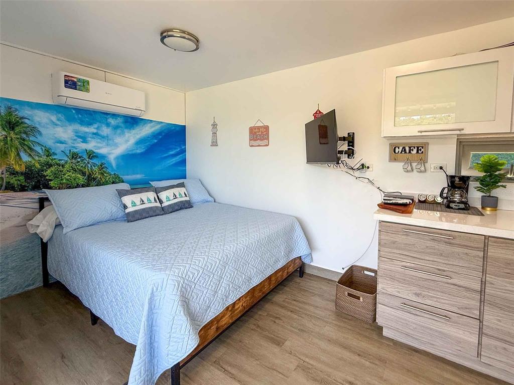 A bedroom features a bed with blue bedding, a wall mural, and a small kitchenette area — 324 CAMINO SOL, VIEQUES, PR