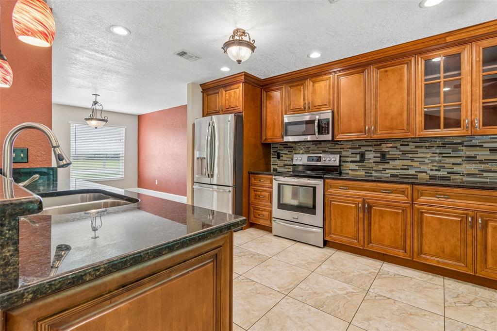 A kitchen features wood cabinets, stainless steel appliances, a dark countertop, and tiled flooring — 15109 SPRINGVIEW STREET, TAMPA, FL