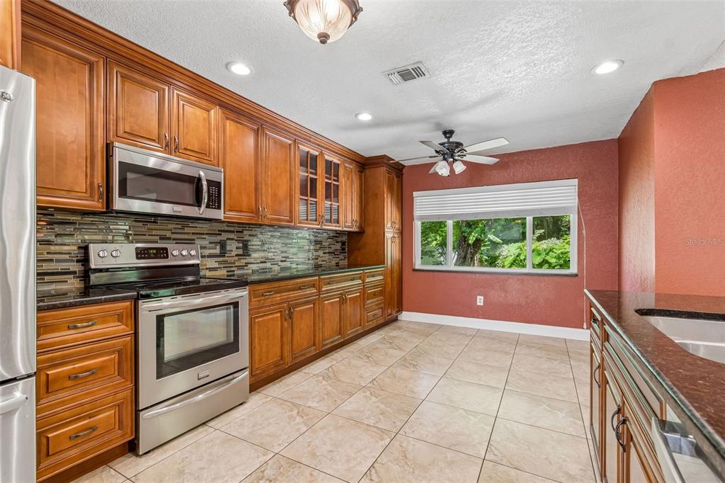 A kitchen with wood cabinets, stainless steel appliances, a tile backsplash, and a windowed dining area — 15109 SPRINGVIEW STREET, TAMPA, FL