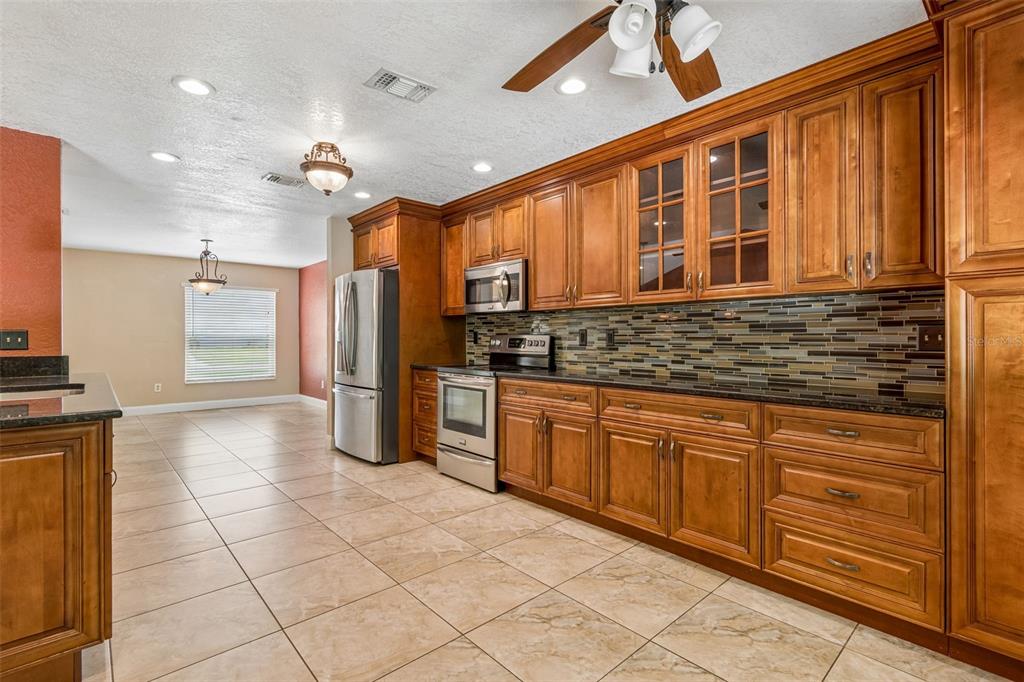 A kitchen features wood cabinets, stainless steel appliances, a tiled backsplash, and light-colored floor tiles — 15109 SPRINGVIEW STREET, TAMPA, FL