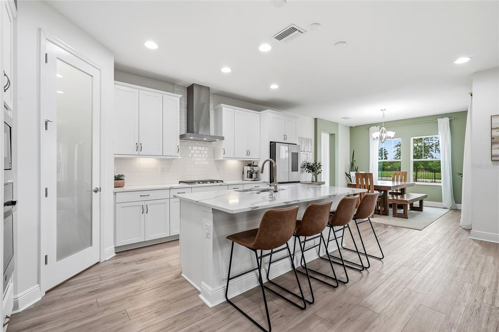 A modern kitchen features white cabinetry, a marble-topped island with bar stools, and wood flooring — 17842 EVERLONG DRIVE, LAND O LAKES, FL