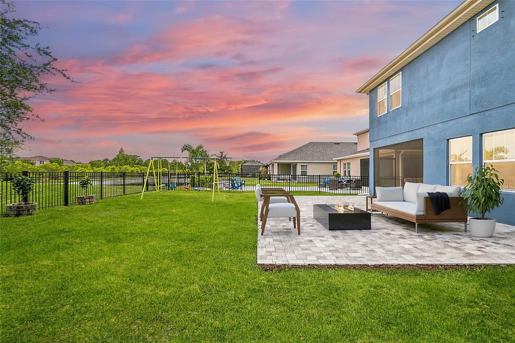 A backyard features a paved patio with a fire pit, outdoor seating, and a swing set — 17842 EVERLONG DRIVE, LAND O LAKES, FL