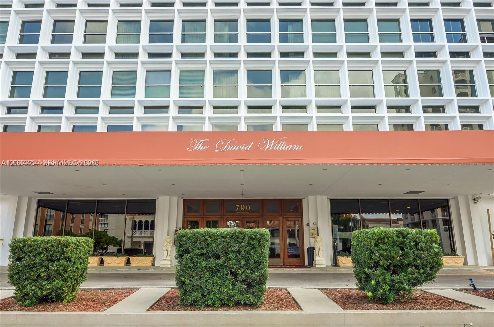 The exterior of a multi-story building features a large orange awning and three manicured hedges — 700 Biltmore Way # 1216, Coral Gables FL 33134, CORAL GABLES, FL