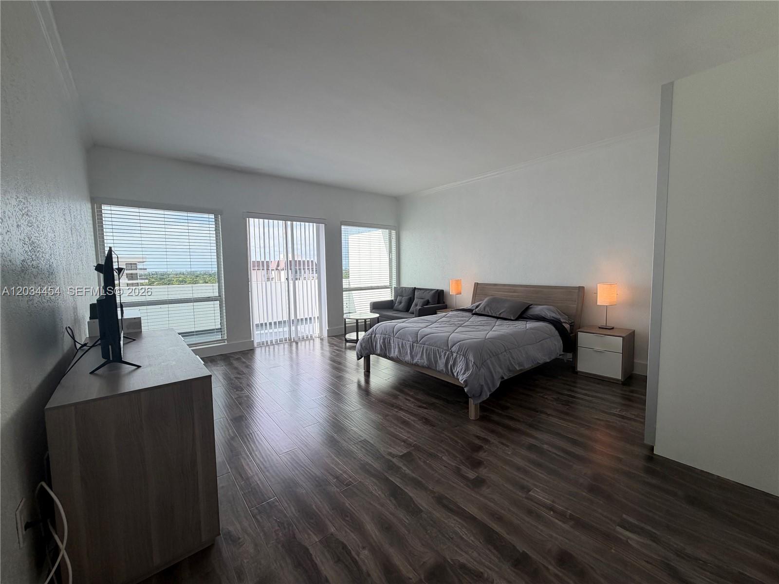 A bedroom features wood-look flooring, a bed, a dresser, and large windows with blinds — 700 Biltmore Way # 1216, Coral Gables FL 33134, CORAL GABLES, FL