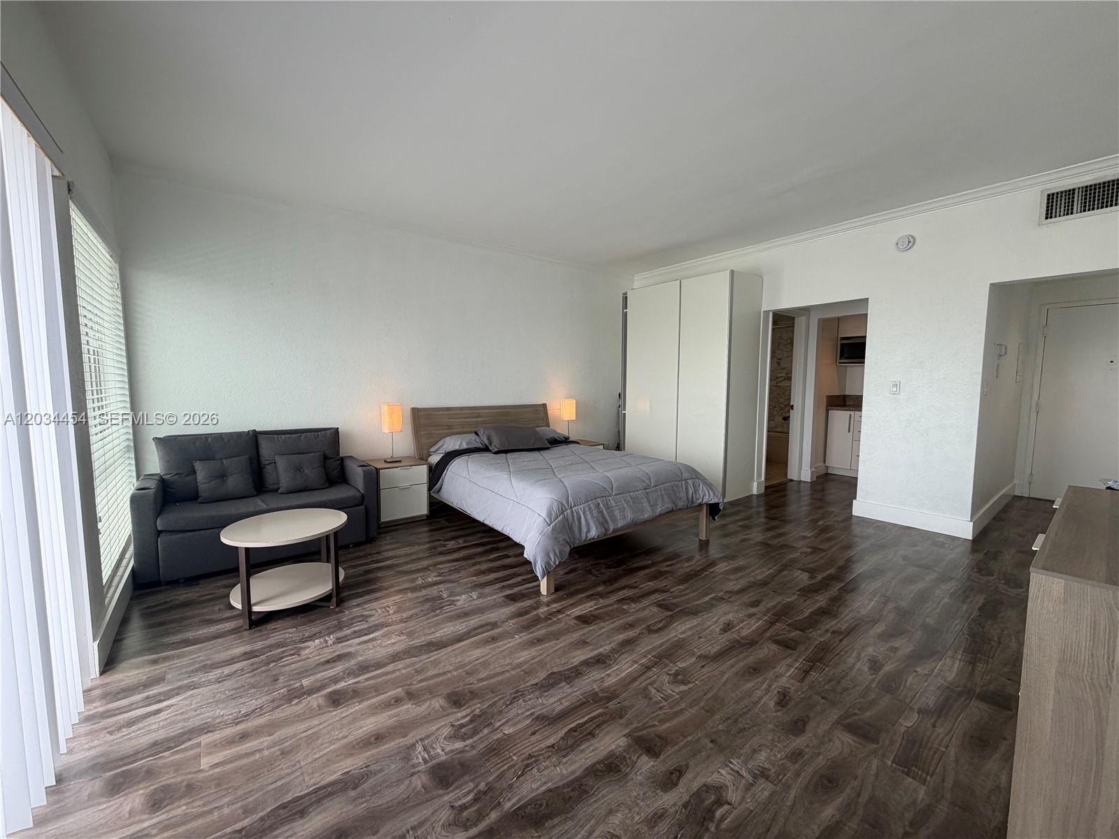A studio apartment features a bed, a gray sofa, and dark wood-look flooring — 700 Biltmore Way # 1216, Coral Gables FL 33134, CORAL GABLES, FL